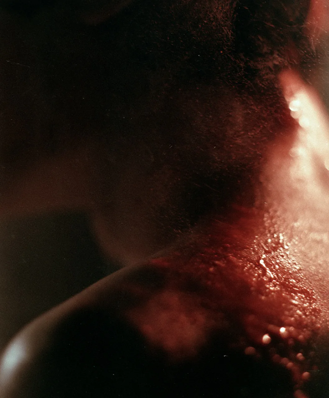 Close-up de cuello y hombro bajo luz roja con gotas.